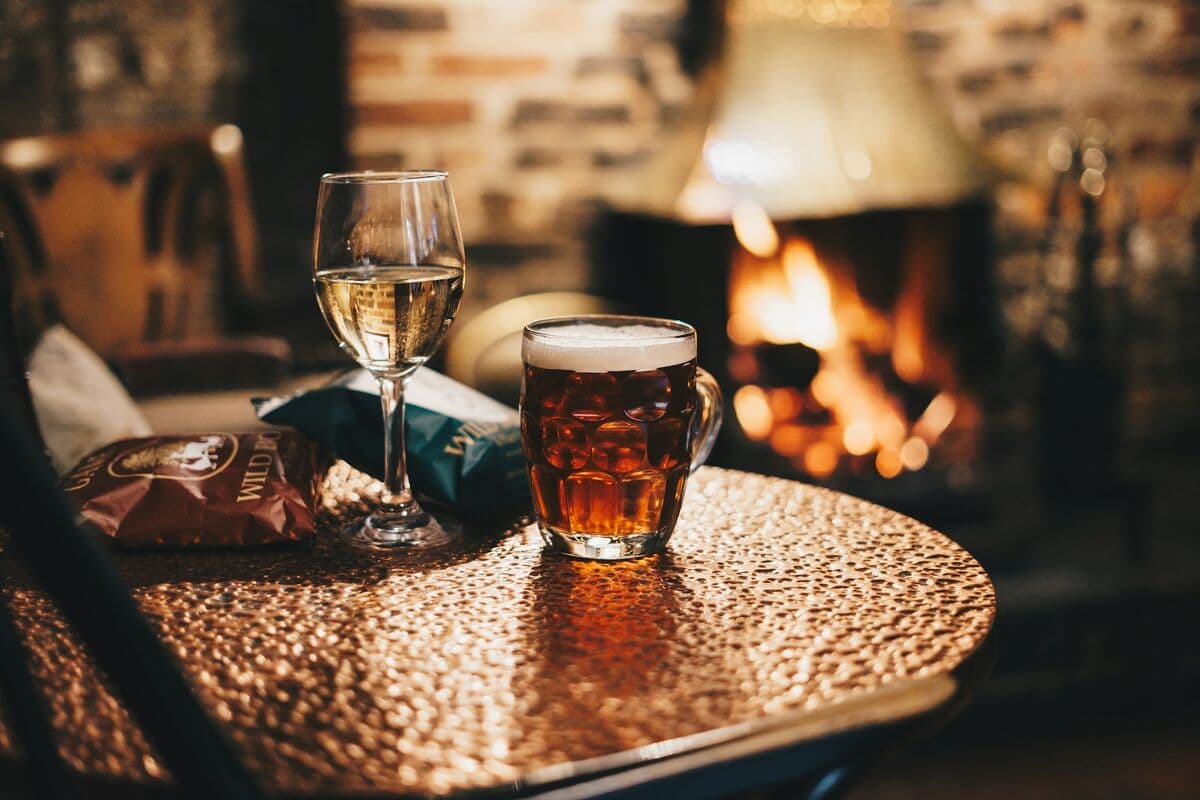 A pint of ale on a table beside a pub fireplace