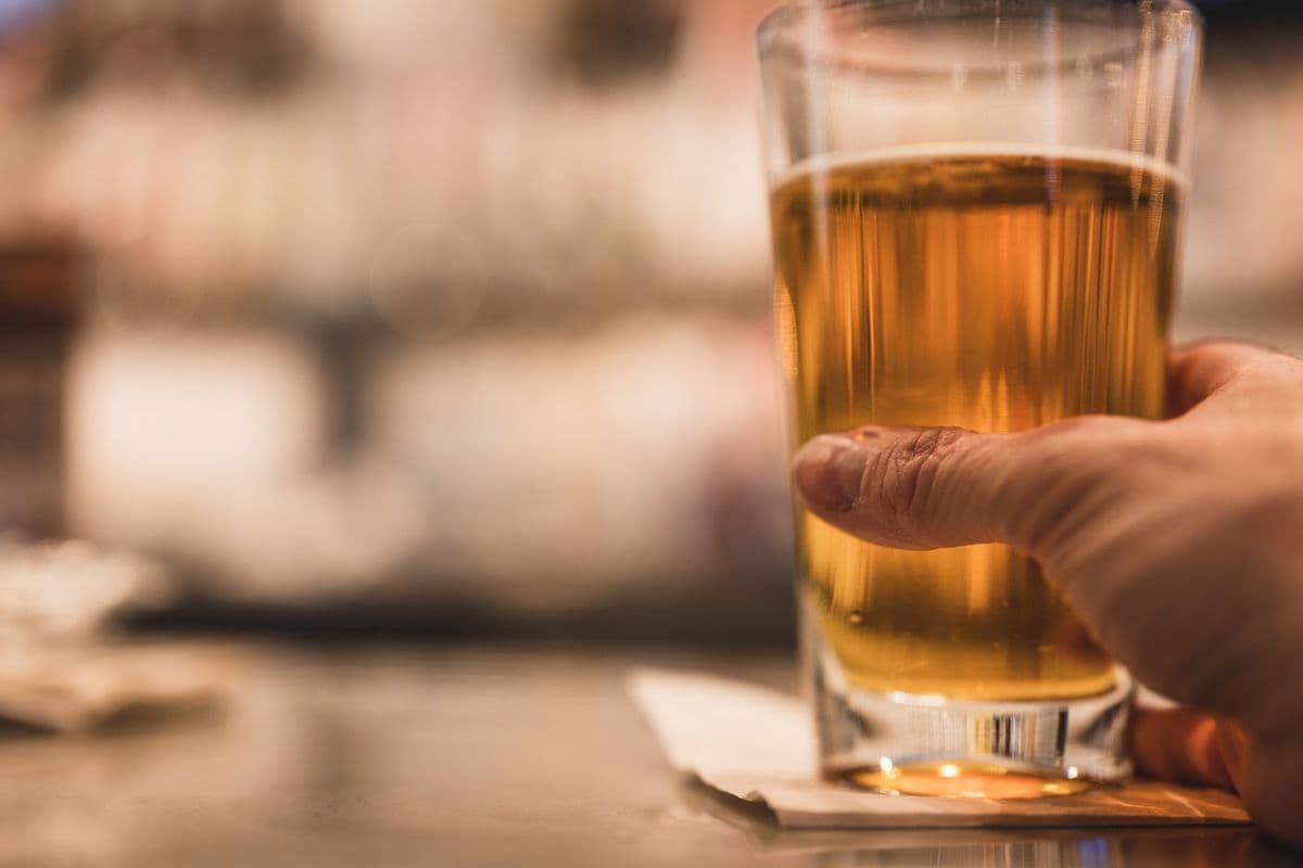 A hand holding a pint of lager in a pub