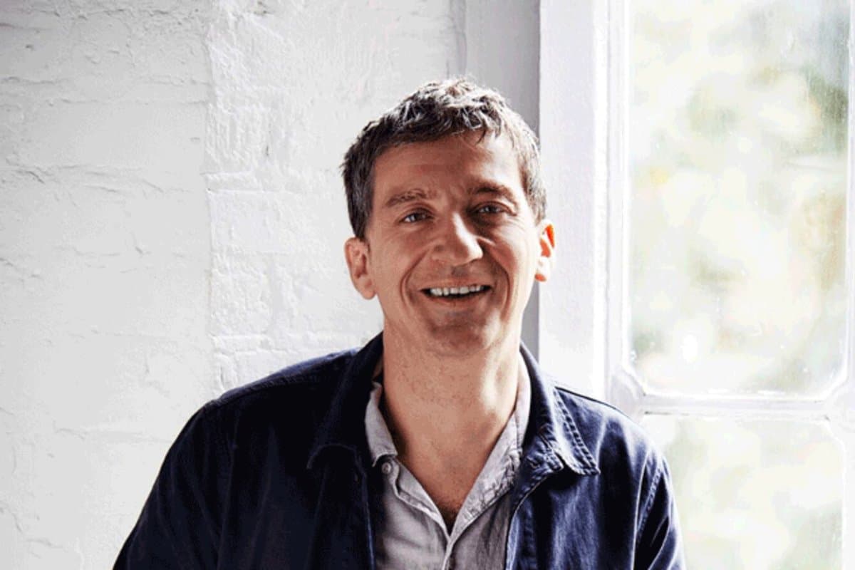 Chef Ben Tish smiling beside a window against a white brick wall