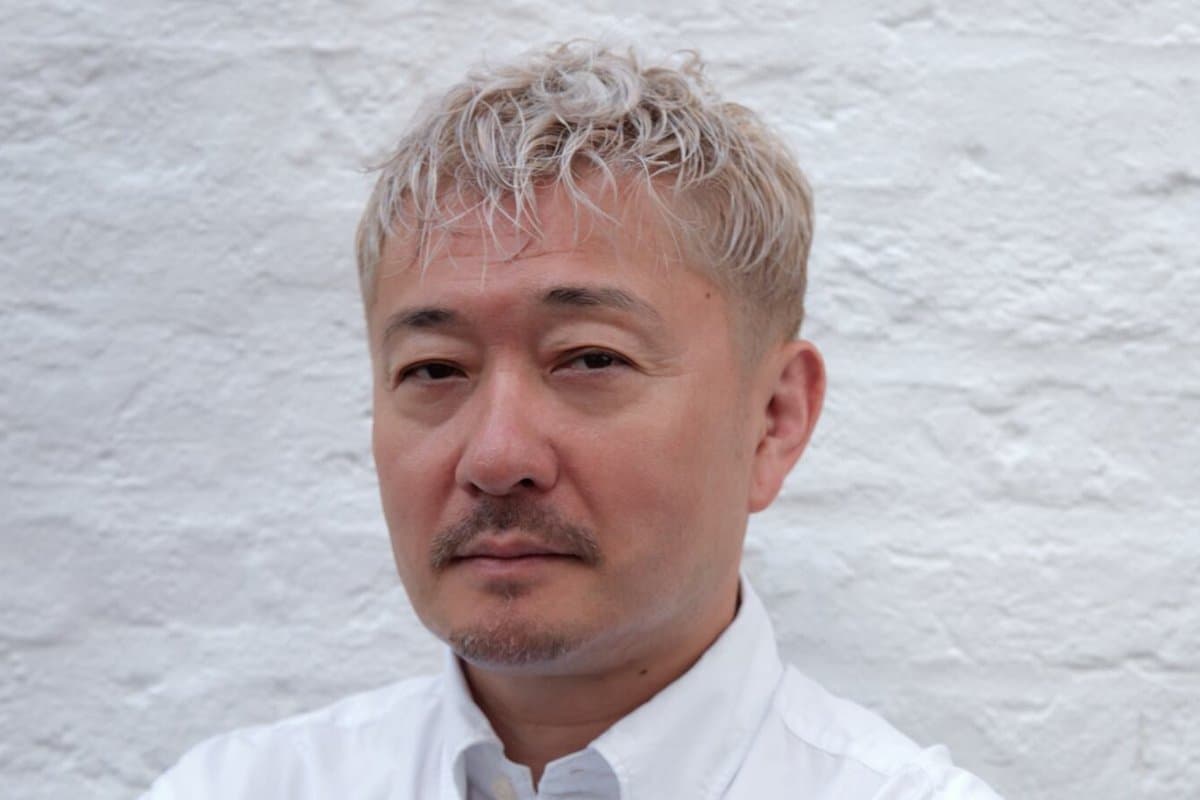 Portrait of sushi chef Endo Kazutoshi in a white shirt against a white brick wall