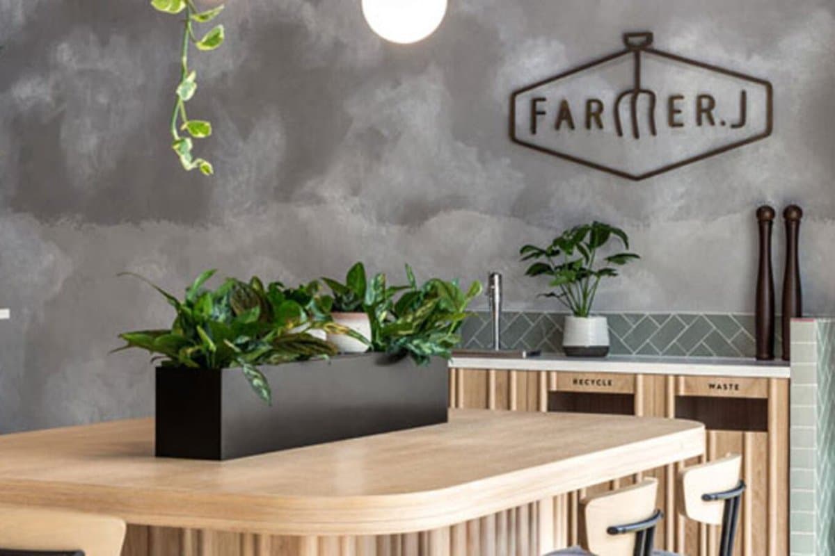 Inside a Farmer J restaurant, with a plant-topped wooden counter and the Farmer J logo on a grey wall