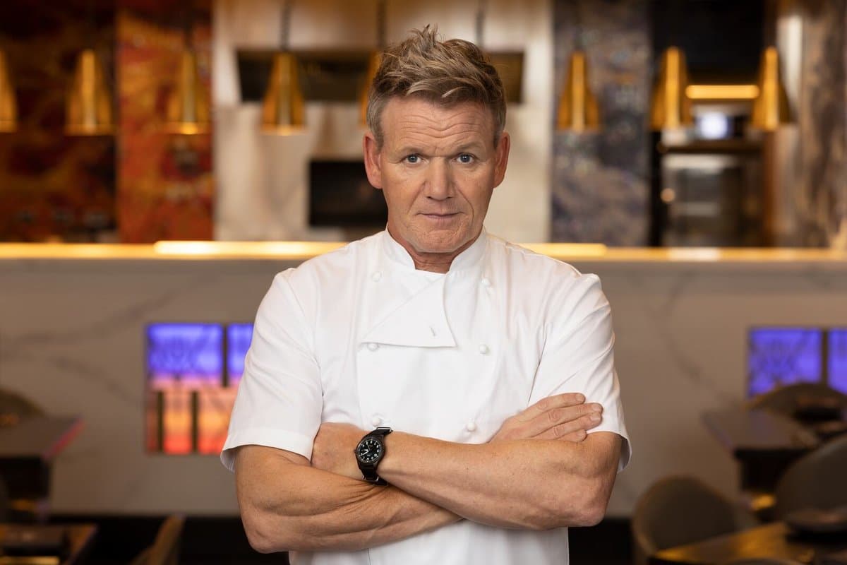 Gordon Ramsay in chef's whites with arms folded inside one of his restaurants