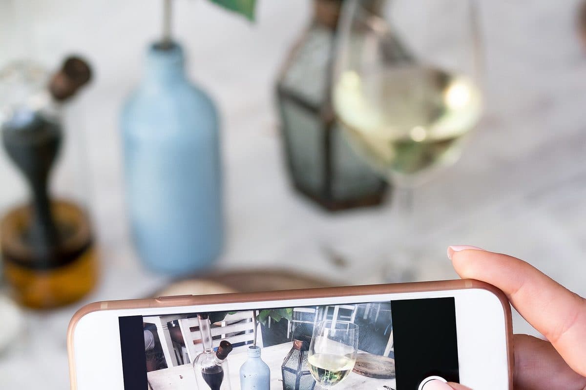 A guest photographing bread and a glass of wine on her phone at a restaurant table