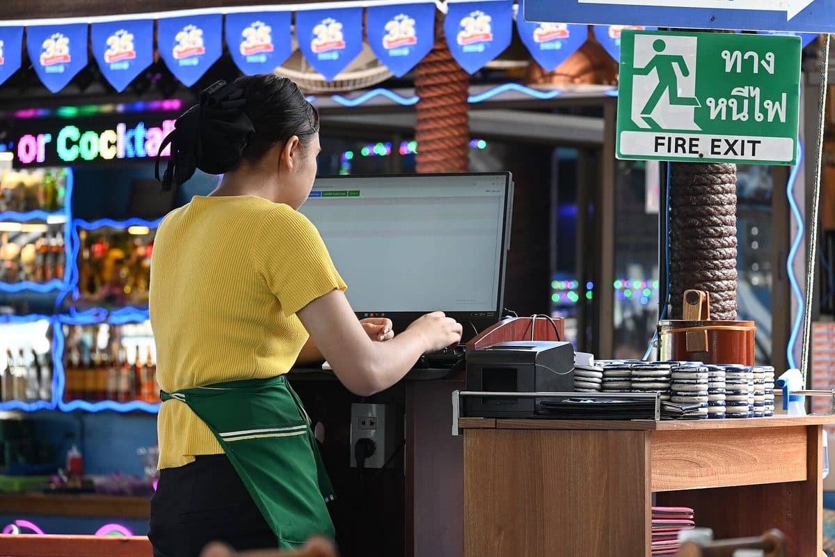 A restaurant server working at a point-of-sale terminal beside a stack of plates