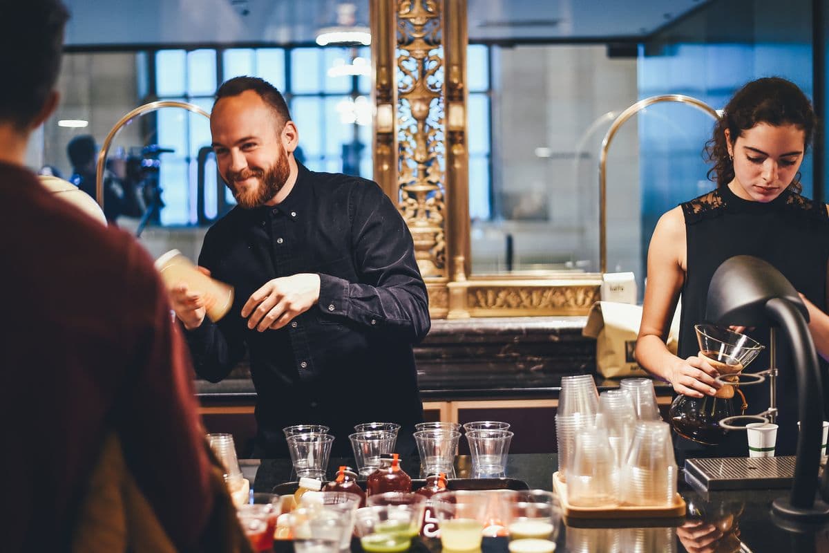 Bartenders pouring a cocktail into a glass at a busy bar