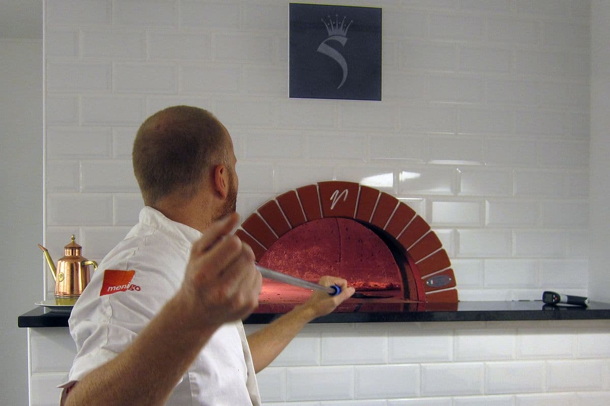 A wood-fired pizza oven with flames inside a restaurant kitchen