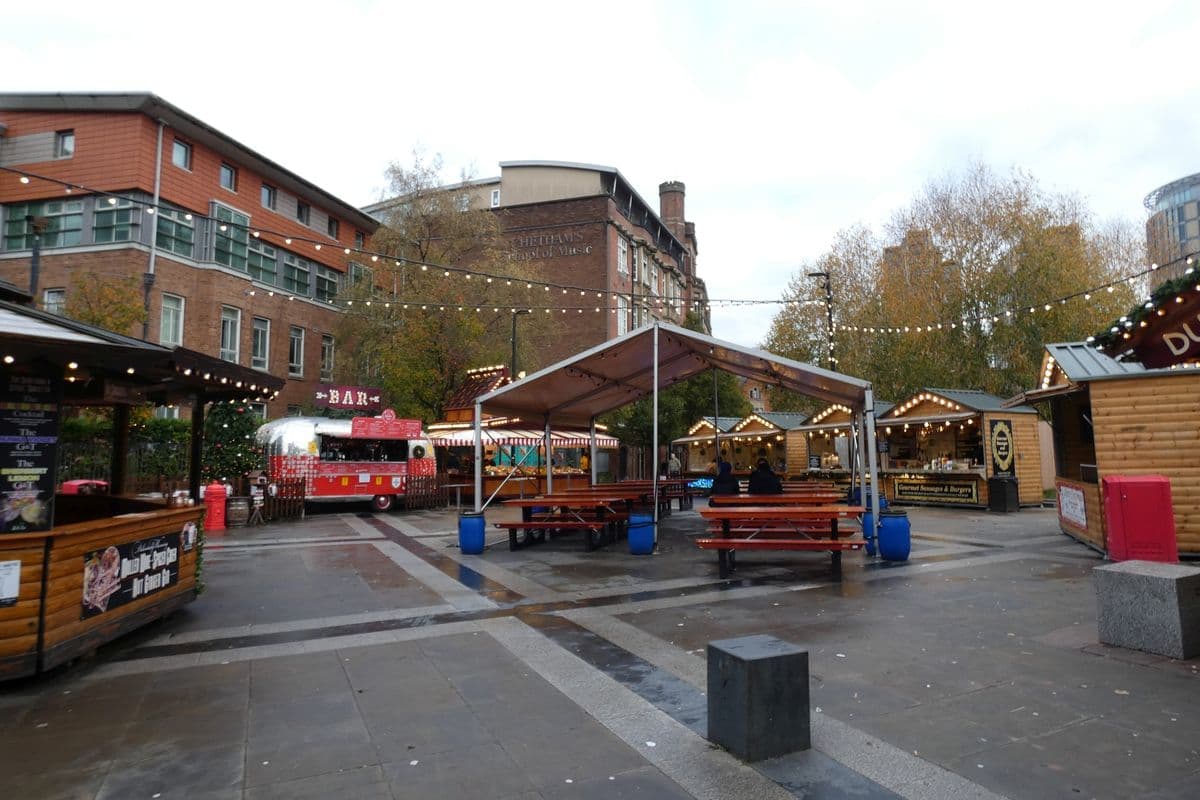 Wooden Christmas market stalls and festoon lights in a square in Manchester city centre