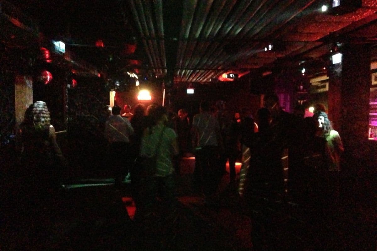 A dimly lit nightclub dance floor with red lights and people standing in groups