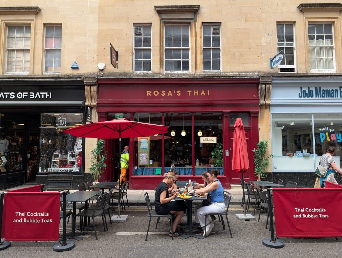The red frontage of a Rosa's Thai restaurant with diners at outside tables