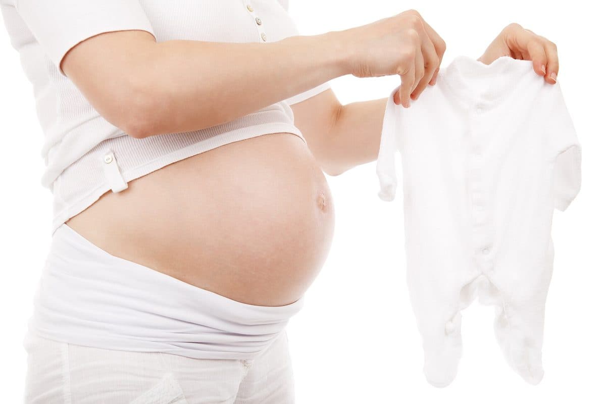 A pregnant woman holding a white babygrow