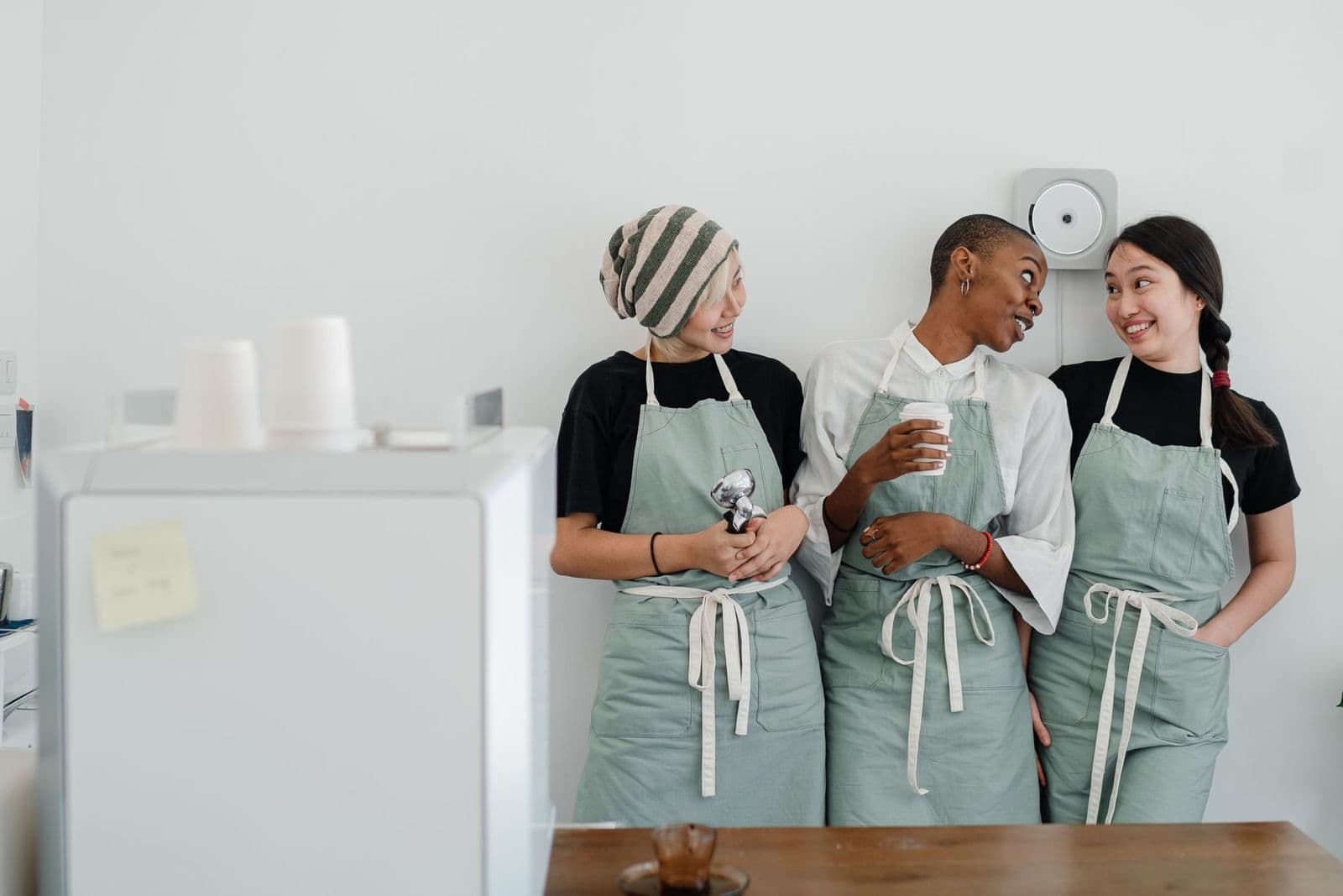 Three cafe staff in aprons chatting behind the counter before service
