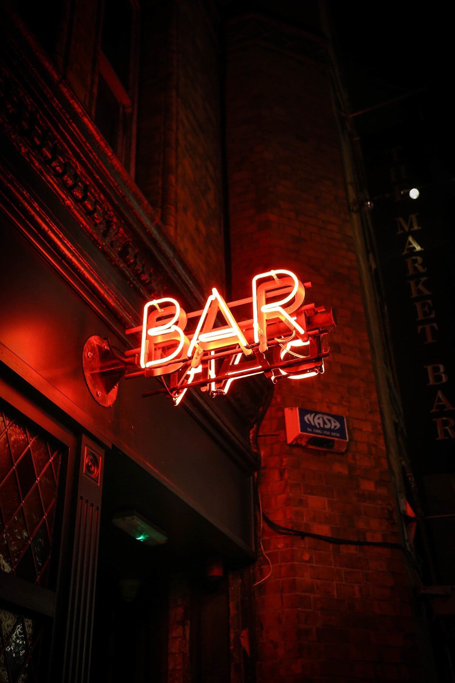 Red neon BAR sign on a brick wall at night