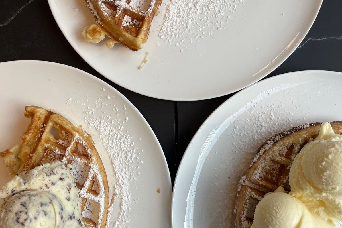 Plates of waffles topped with ice cream and sauce on a table
