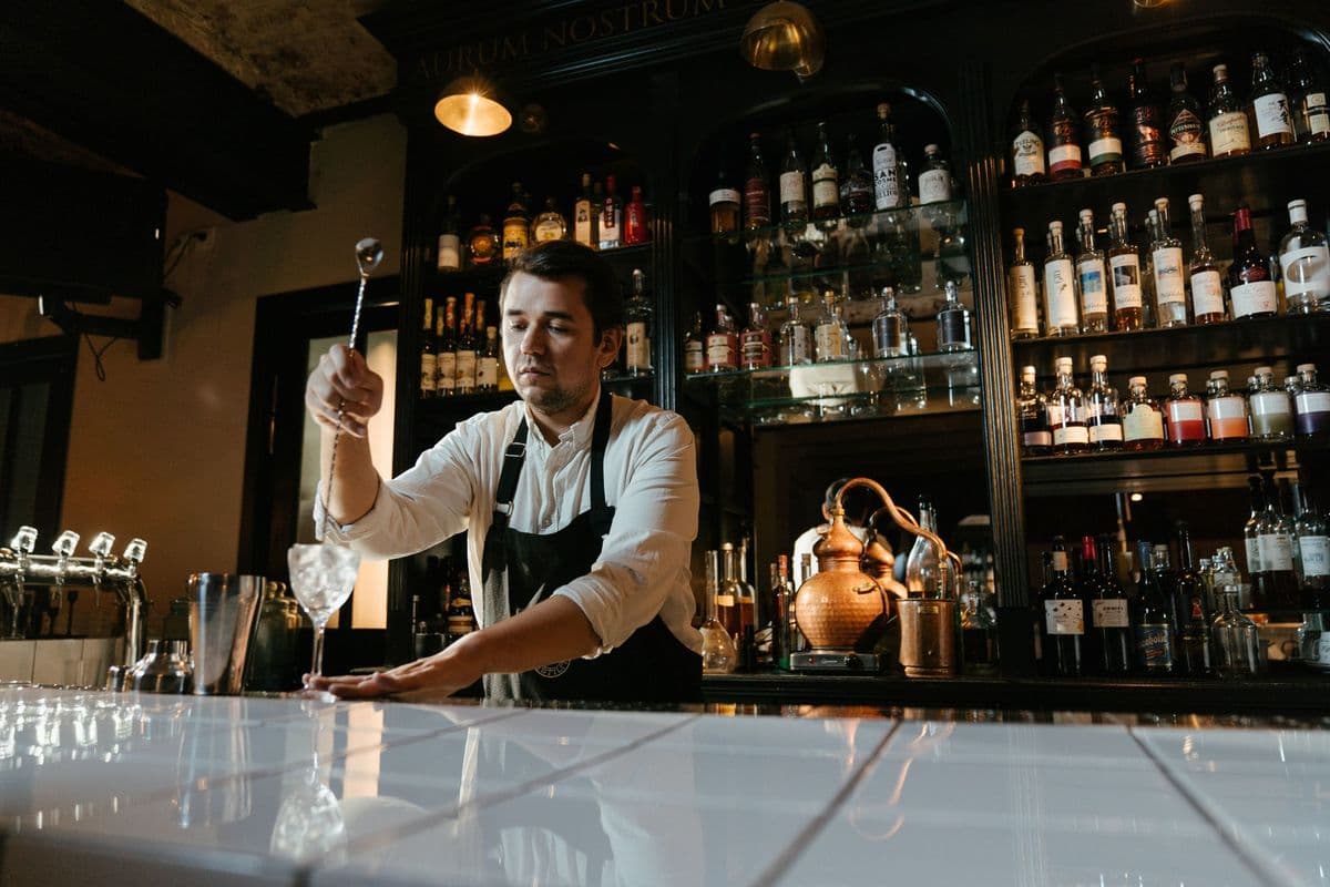 A bartender in a white shirt mixing a drink behind a well-stocked bar