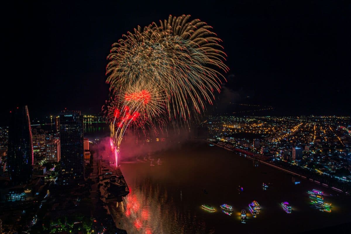 Fireworks bursting over a river and a city skyline at night