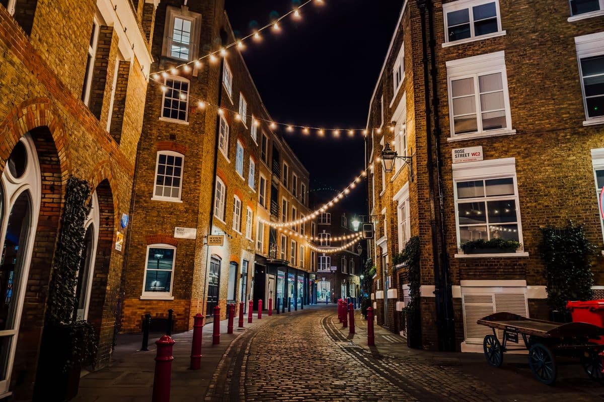 String lights above a narrow cobbled street in Soho at dusk