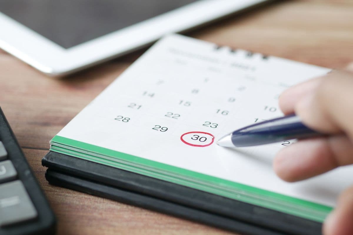 A hand circling a date on a desk calendar with a pen