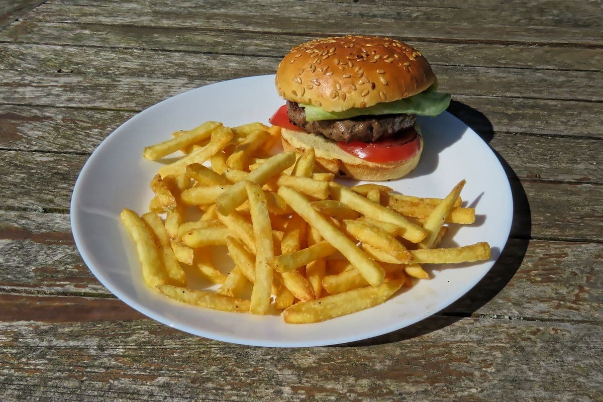 A burger in a sesame bun with a plate of chips on a wooden table