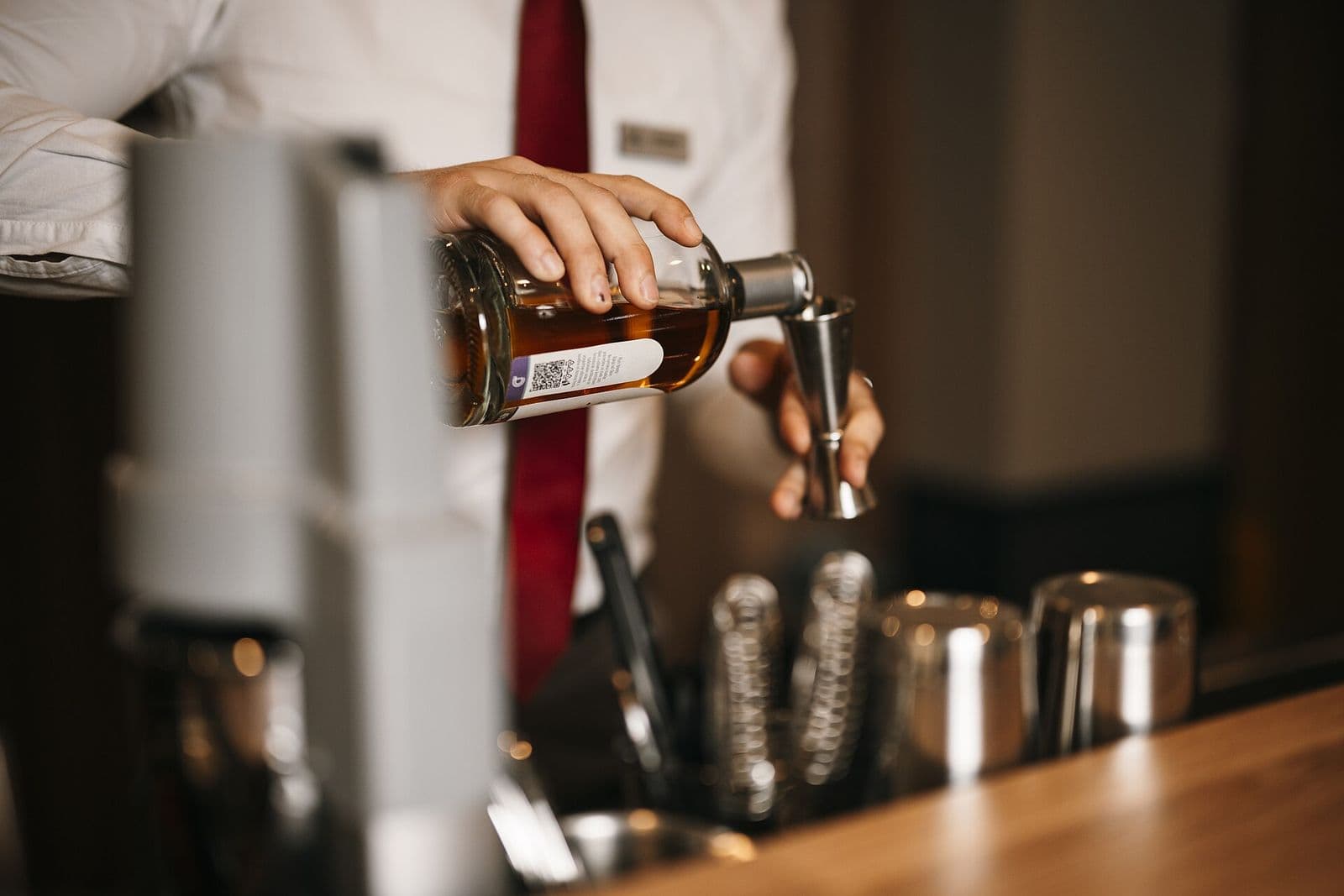 A bartender in a white shirt pours a spirit into a measure behind a bar