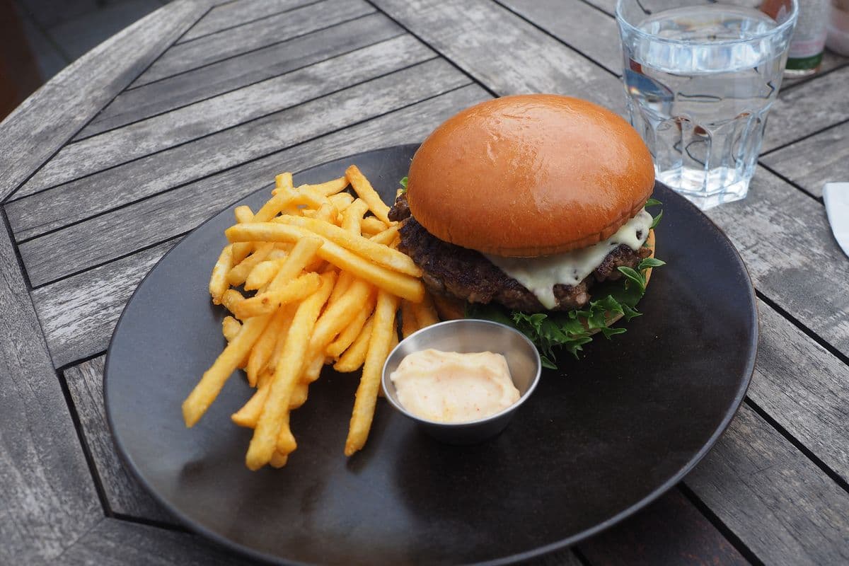 A cheeseburger with fries and a dip on a wooden table