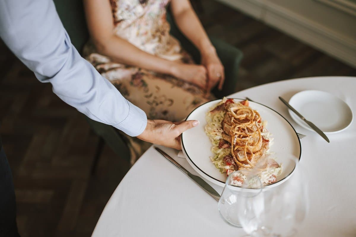 A plate of pasta being served to a guest at a restaurant table