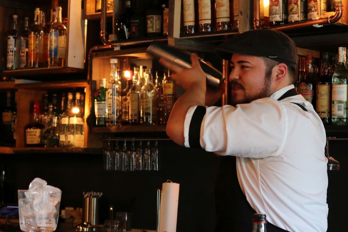A bartender shaking a cocktail behind a well-stocked bar