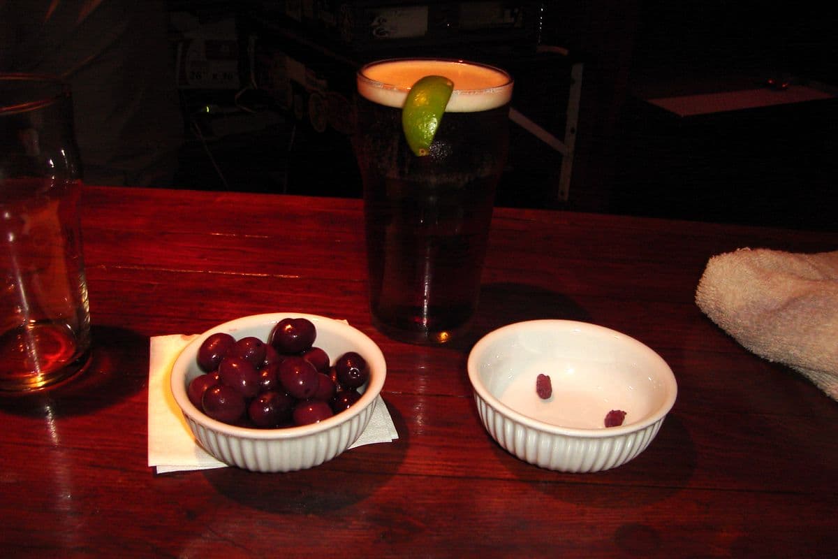 A pint of beer on a pub table next to a bowl of olives