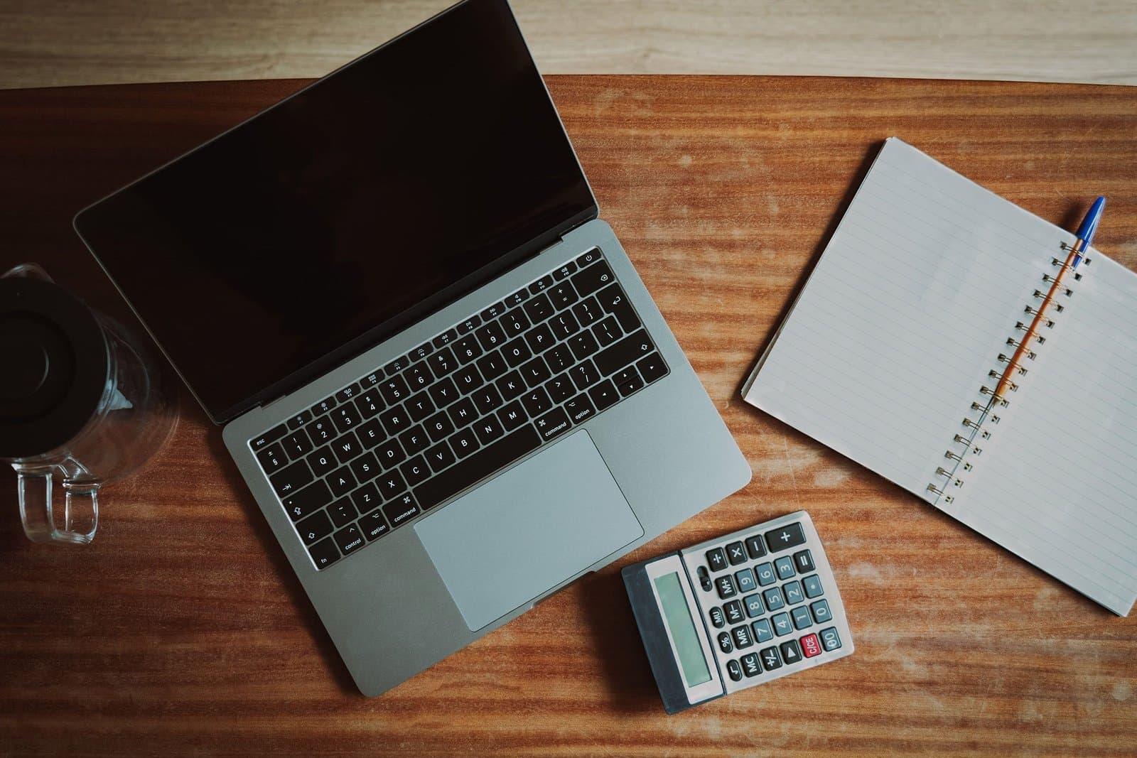 Top view of a desk with a laptop, calculator and open notepad