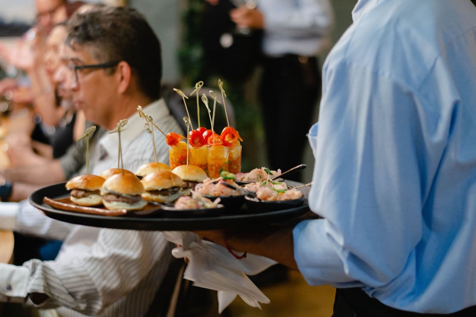 Server carrying a tray of small plates through a busy dining room