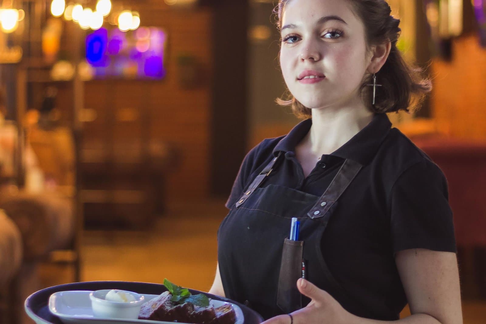 A waitress in uniform carrying a tray of food in a warmly lit restaurant