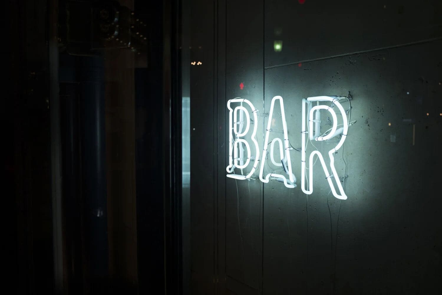 White neon BAR sign on a dark wall